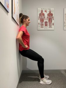 Woman performs a wall sit exercise with back against wall and knees bent